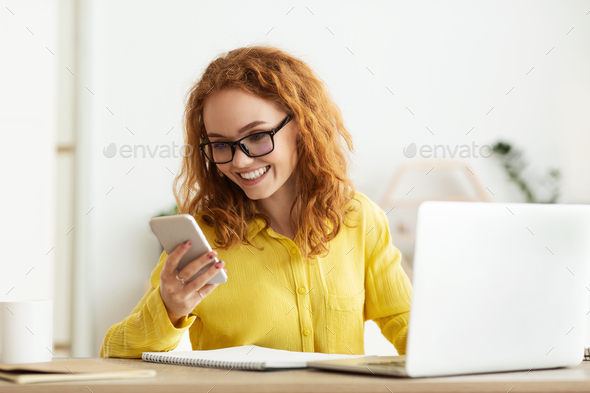 Businesswoman checking message on cellphone, working on laptop - Stock Photo - Images