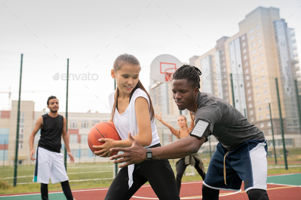 African basketballer keeping his hand by ball held by female player