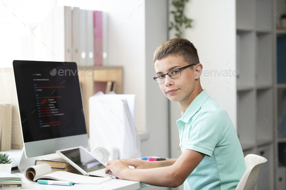 Serious middle school student sitting by desk in front of computer monitor