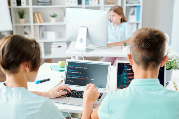 Two schoolboys and schoolgirl sitting by desks in front of computers - Stock Photo - Images