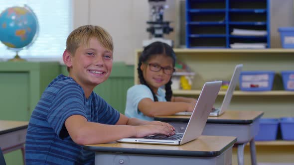 Portrait of two kids in school classroom with laptop computers alt