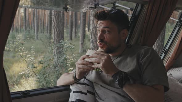Hipster Man Enjoying Sandwich in Camper in Forest alt
