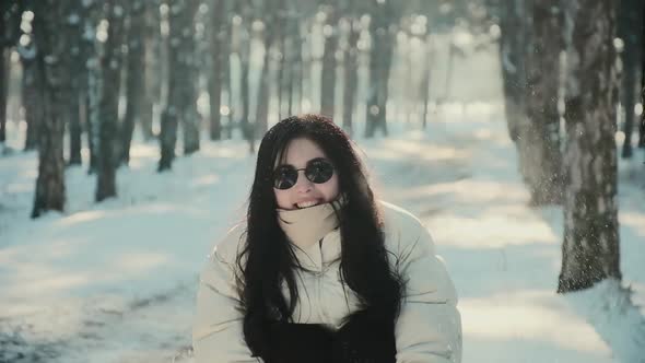 Pretty Woman with Sunglasses Throws Snow in Winter Forest