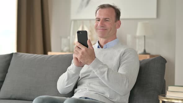 Middle Aged Businessman Celebrating Success on Smartphone on Sofa  alt
