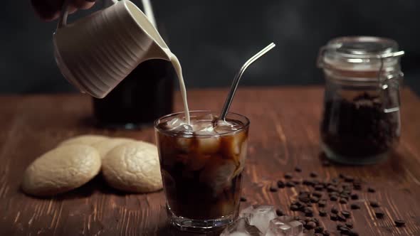 Slow Motion of Cream Being Poured Into a Glass of Cold Brew Iced Coffee on Brown Wood Table with