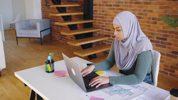 Islamic Woman in Hijab Works with Laptop While Sitting at Her Desk at Home alt
