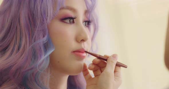 Close-up On Lips Of A Young Asian Woman. Makeup Artist Apply Lipstick To Model. alt