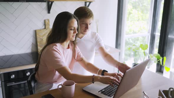 Couple Uses Laptop at Wooden Table in Brightly Lit Kitchen