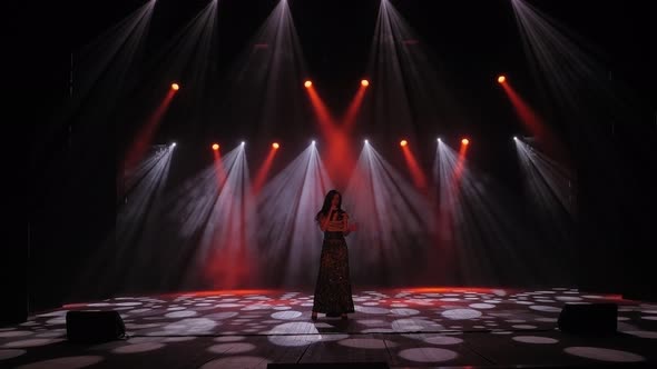 A Girl Sings a Song on Stage in the Dark Under the Light of Flashing Floodlights alt