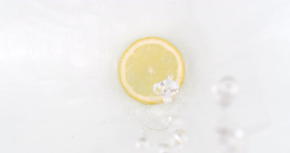 On a White Background, a Splash of Water Falls on a Slice of Lemon in Slow Motion alt