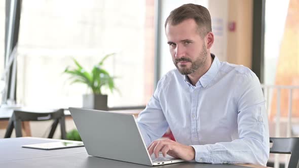 Cheerful Young Man with Laptop Pointing with Finger alt