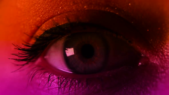 Extreme Closeup View of Woman's Opening Beautiful Eye in Dark in Neon Light