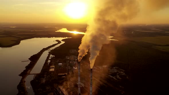 Top view on two pipes with smoke. Factory on the natural fields background at sunset. alt