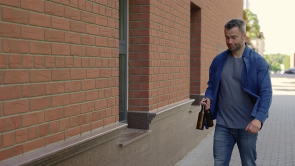 Man is Holding Two Glass Bottles and Put Them to the Sorting Bin for Glass alt