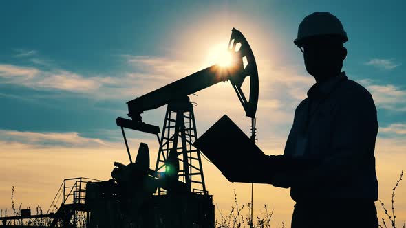 Male Engineer and a Functioning Pumpjack in Sunlight. Oil and Gas Industry Concept. alt