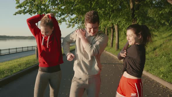 Doing Sport Together. Three Friends Stretching Muscles Before Jogging Along the Embankment of the alt