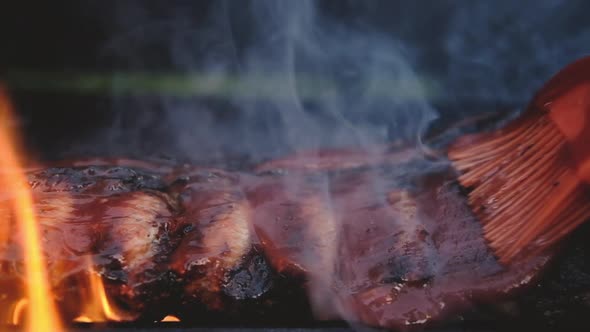 Close-up of ribs fried on grill in flame poured with sweet BBQ sauce
