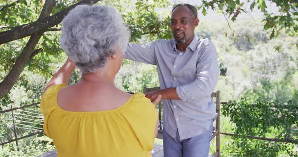 Senior African American husband and mixed race wife dancing and laughing together in the garden alt