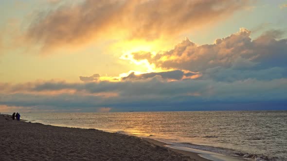 The dawn between the clouds breaks the sun on the beach on the sea - Sand, people and sun rays