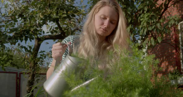 Young Girl with a Watering Can Watering Flowers in a Summer Garden