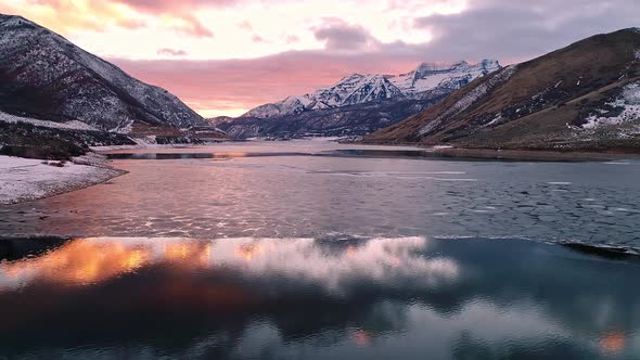 Flying toward colorful sunset over partial frozen lake in Utah alt