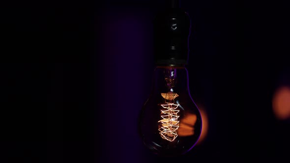 A light bulb hangs in the dark and pulses with light close up.