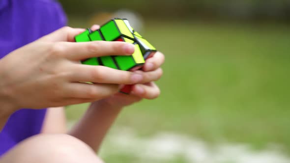 Boy is playing with popular rubik's cube outdoors. Smart kid develops his logic alt