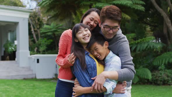 Smiling asian parents hugging happy son and daughter in garden alt