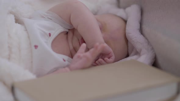 Pretty Newborn Baby Girl Moving Hands Waking Up in Cozy Bed with Book Lying at Front alt