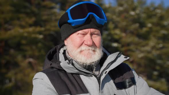 Life After Retirement Cheerful Old Man in Hat and Ski Goggles Backdrop of Snowy Forest in Sunny