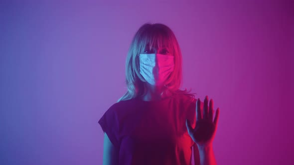 Woman in Medical Mask Looking at Camera and Slides Her Palms on Glass alt