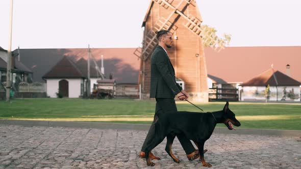 A Rich Businessman in a Business Suit Walks with a Large Doberman in the Park alt