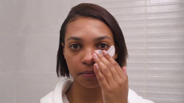 A Young Woman with Dark Skin Uses White Patches for the Eyes Against Wrinkles