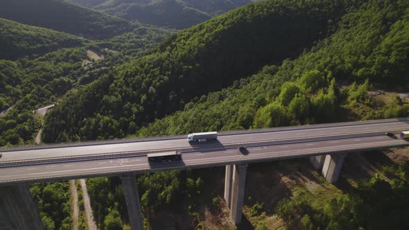 Aerial View of White Cargo Semi Truck Driving on Two Way Motorway Viaduct Over Green Hills alt