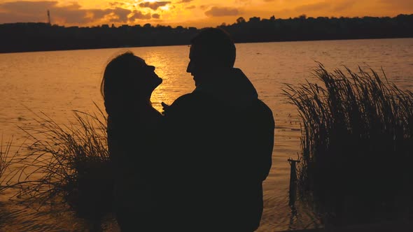 Beautiful Silhouette of Romantic Couple Resting in Caresses at Evening Lake alt