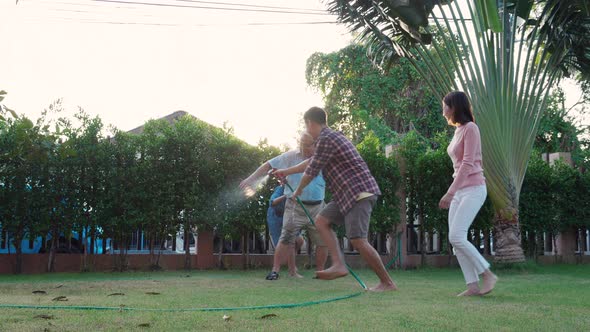 Happy Family playing together during Retired Grandfather watering the plants at the home garden. alt