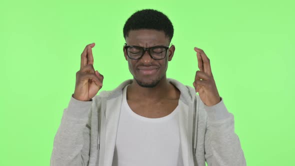 African Man Praying with Fingers Crossed on Green Background alt