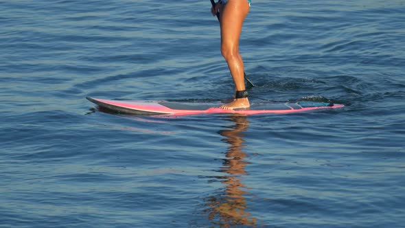 A young woman SUP surfing in a bikini on a stand-up paddleboard surfboard. alt