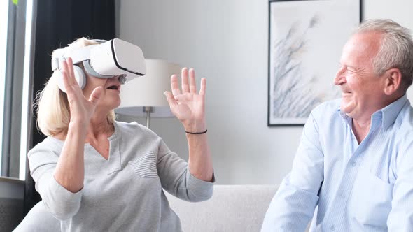 Happy Senior Man and Woman Wearing Virtual Reality Headset at Home Sitting on Sofa alt