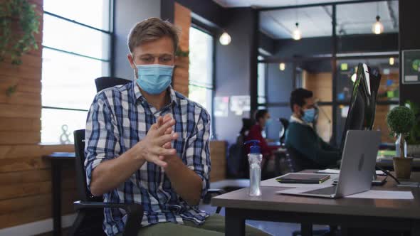 Caucasian man wearing face mask using hand sanitizing at modern office alt