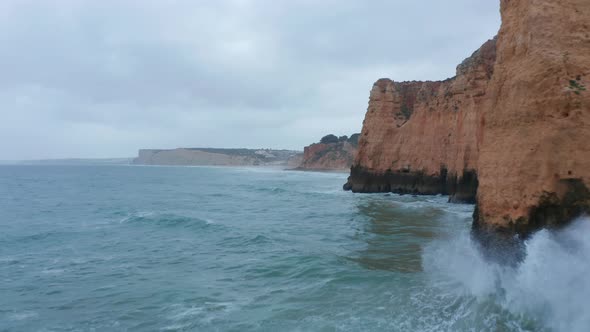Aerial Drone Flying Low Above Ocean Waves By High Orange Colored Cliffs Lagos Algarve Portugal Dolly alt