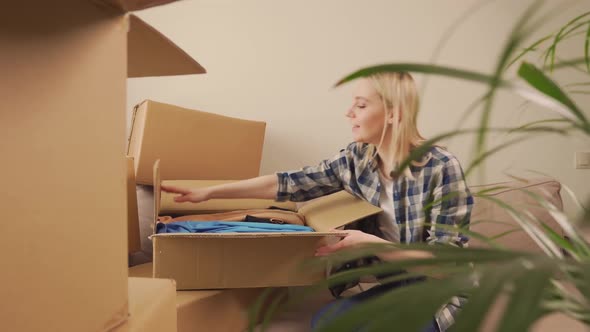 A Woman Sitting on a Sofa Takes Out Clothes From a Cardboard Box After Moving in