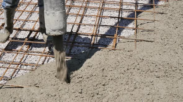 A Male Builder Directs the Flow of Concrete Mix From a Thick Hose of a Concrete Pump While Pouring a