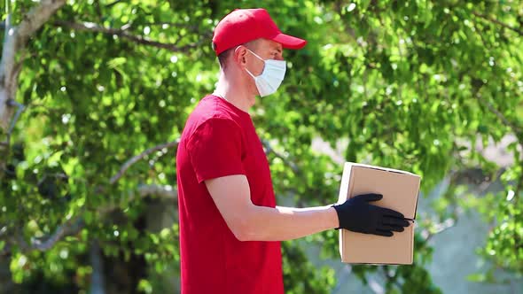 A delivery worker in red uniform holds out cardboard boxes in medical rubber gloves