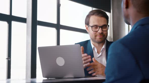 Young businessman in a suit interviewing a african american man at the desk alt