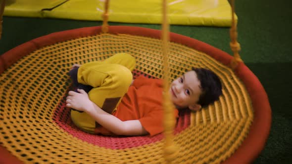 A Boy Swings on a Suspended Carousel Lying on His Back