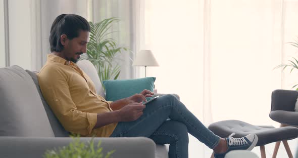 Man sitting on the couch at home and using a tablet