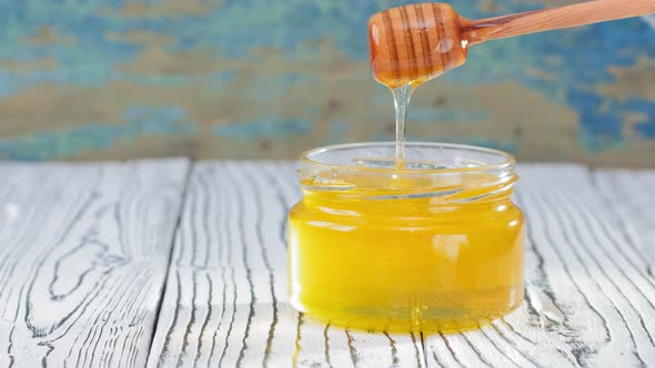 Honey in Glass Jar with Honey Dipper Over Rustic Wooden Background alt