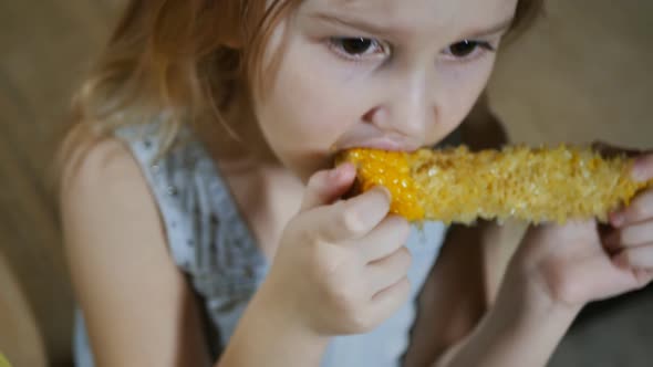 A Teenage Girl Eats Boiled Corn and Looks Attentively at the Screen