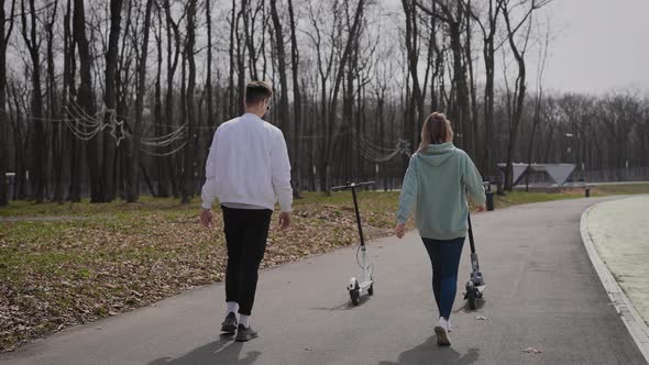 A Beautiful Couple of Young People Ride in the Park on Electric Scooters alt